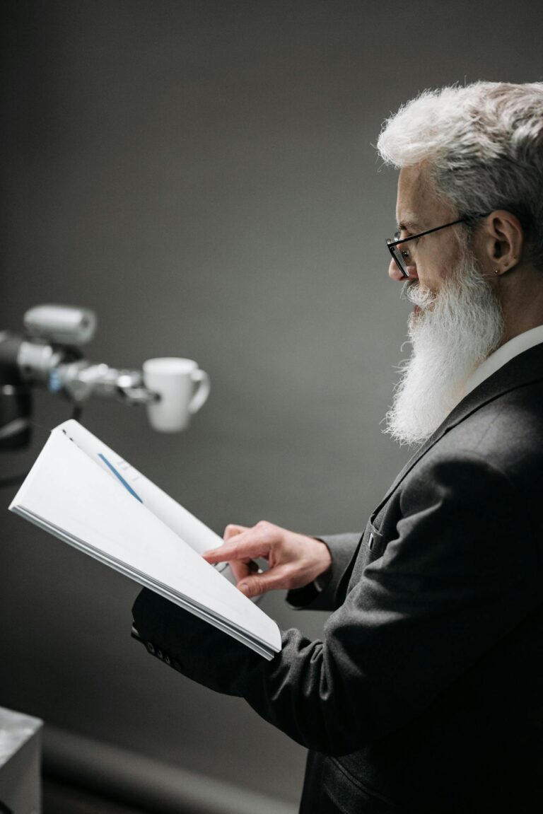 A scientist observes a robotic device while holding documentation in a lab.